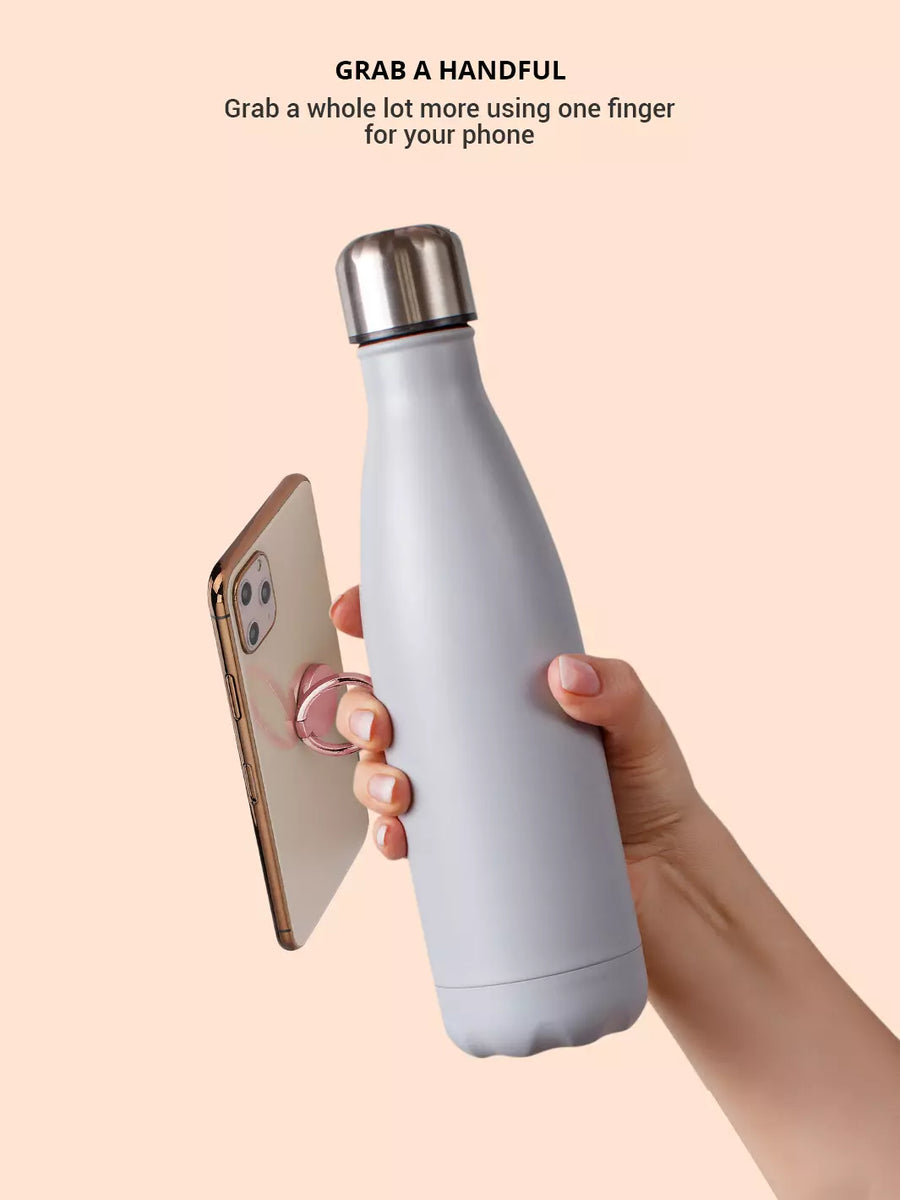 Holding the iPhone with one finger through the rose gold phone ring while grabbing a tumbler