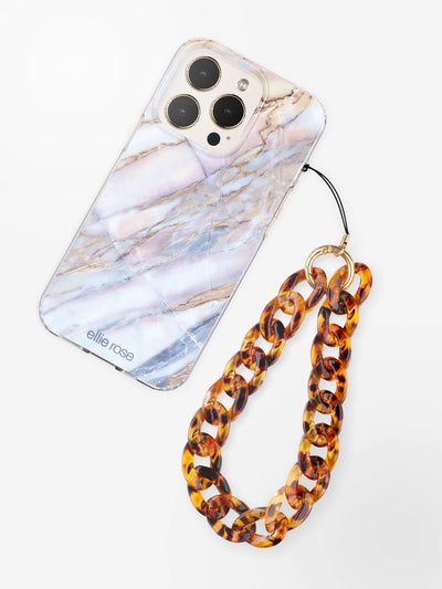 Tortoiseshell phone wristlet charm with gold metal ring attached to iPhone with desert marble case