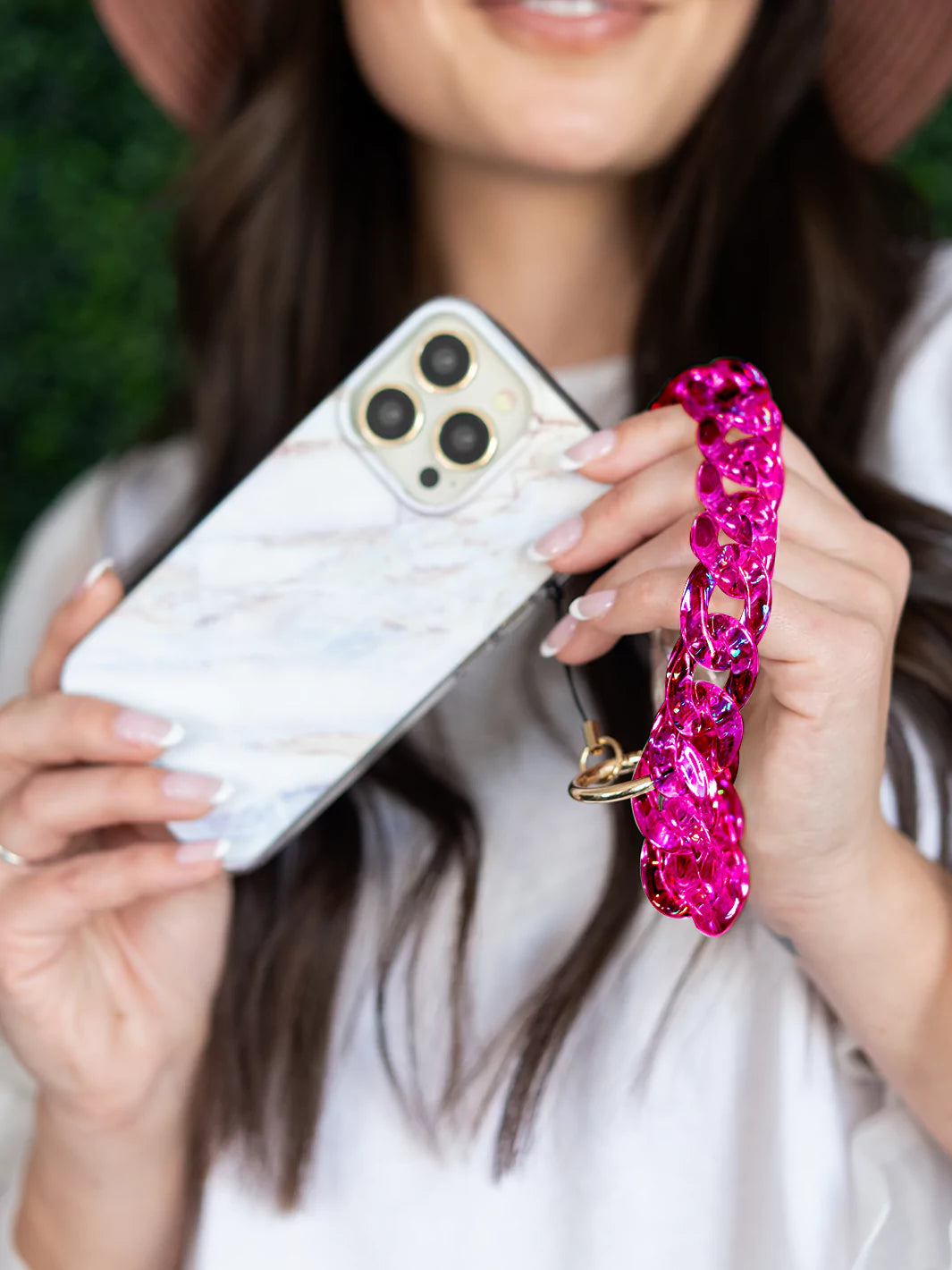 Hot pink clear holographic phone charm wristlet showing iPhone with desert marble case with green background wallpaper and white dress