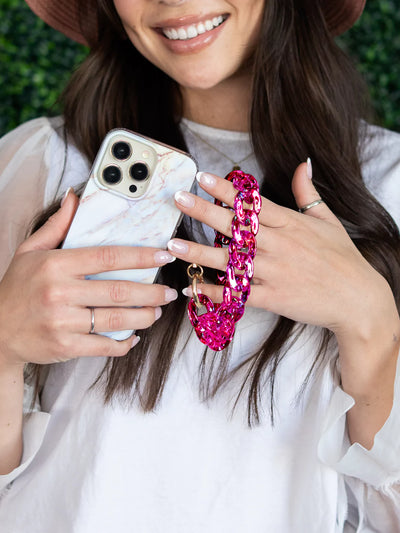 Showing iPhone and pink holographic phone charm wristlet together on both hands while smiling