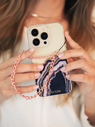 iPhone case holding on right hand connected with Rose gold phone wristlet charm with yelllow and gray background