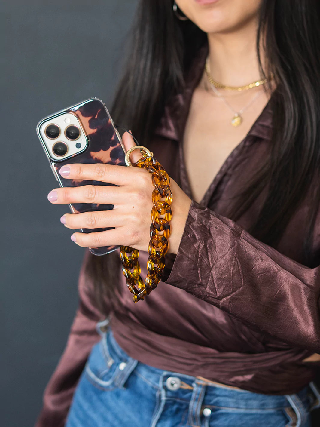 Showing Tortoiseshell phone wristlet charm and iPhone with gold metal ring wearing brown top and blue jeans and gold neclace