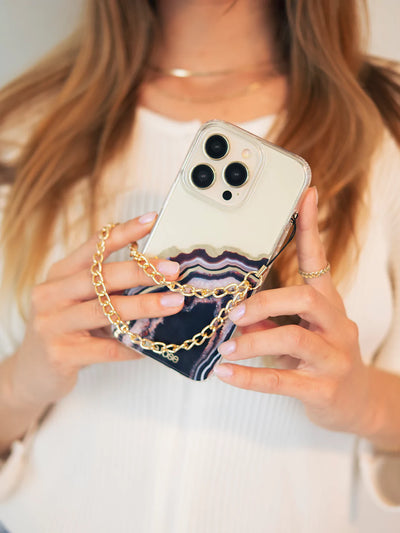 Showing gold phone wristlet charm connected to iPhone with black agate case and blonde hair as background