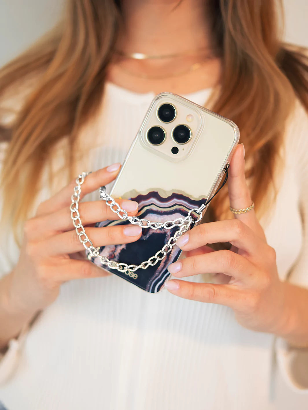 Showing silver phone wristlet charm connected to iPhone with black agate case and blonde hair as background